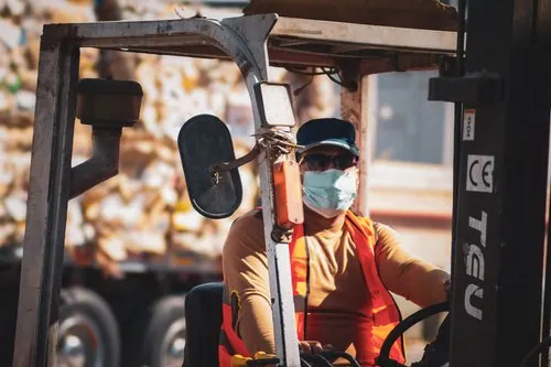 Forklift operator wearing a face mask and reflective vest